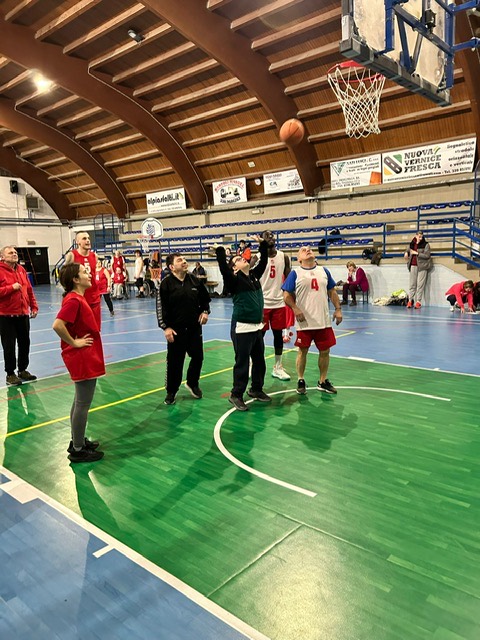 Azione di tiro: il pallone &egrave; in aria verso il canestro e i giocatori delle due squadre, in rosso e in bianco, seguono la traiettoria.